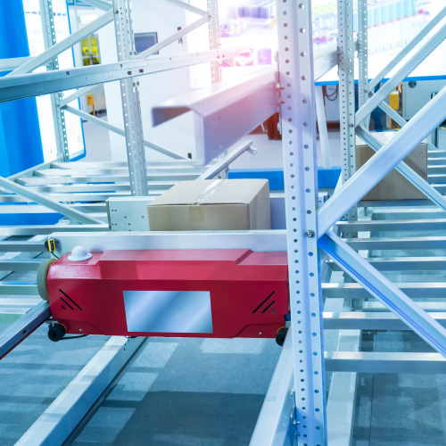 Red shuttle robot retrieving cardboard box from metal racking