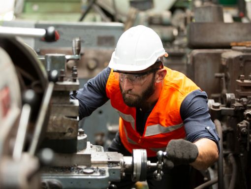 Man in white hard hat and safety vest operating a cutting machine