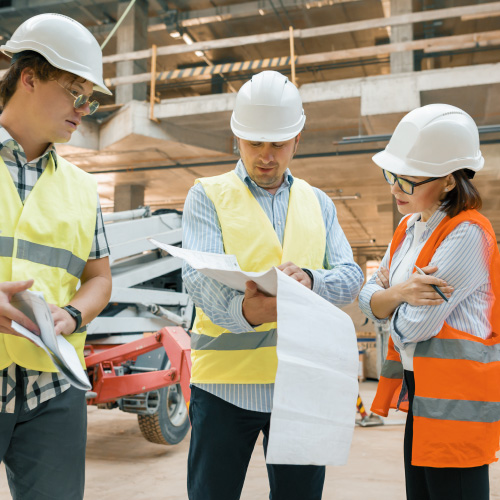 Three people in safety vests looking at documents in warehouse construction zone