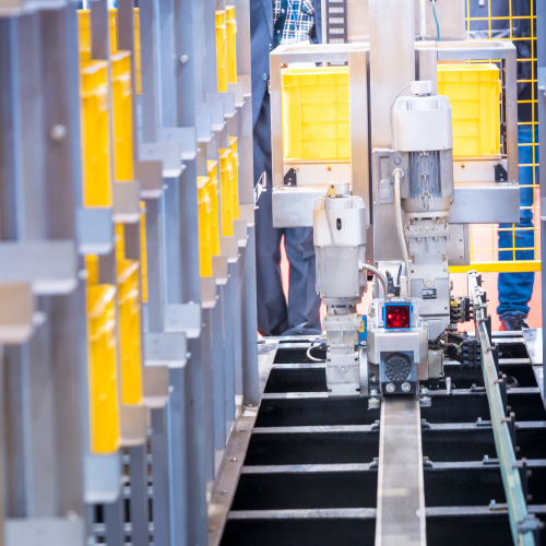 Shuttle system on metal track between two tall racking systems containing yellow totes